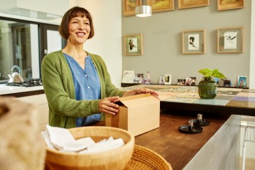 Woman smiling while holding a parcel in her kitchen 